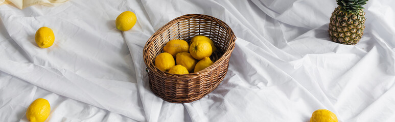 high angle view of ripe lemons in wicker basket near pineapple on white bed sheets, banner