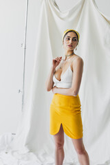 brunette woman in yellow skirt and crop top posing on white