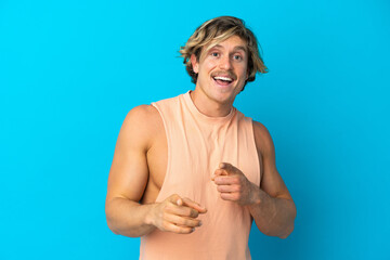 Handsome blonde man isolated on blue background surprised and pointing front
