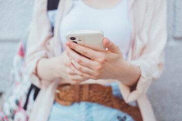 Young blonde woman using smartphone in hand, outdoor hipster portrait, street style, glasses, happy face, backpack, earphones, jacket