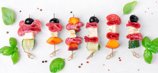 Mini skewer appetizers with salami, feta cheese, olive, peach and cucumber on the white table. Flat lay. Party food