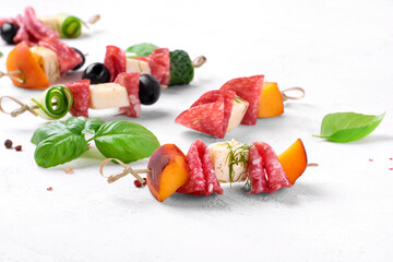 Mini skewer appetizers with salami, feta cheese, olive, peach and cucumber on the white table. Party food