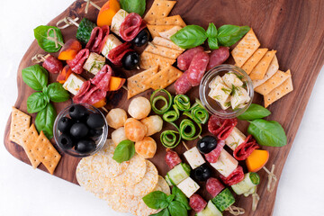 Appetizer assortment on the wooden board. Skewer appetizers, crackers, cheese, cucumber, salami, olives and basil. Party food