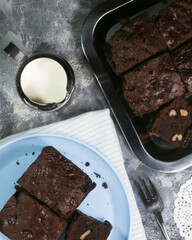 Top view of brownies in a rustic blue background on a metal tray and a blue plate with a jar of milk
