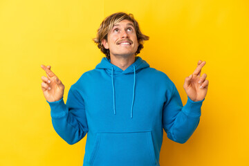 Handsome blonde man isolated on yellow background with fingers crossing and wishing the best