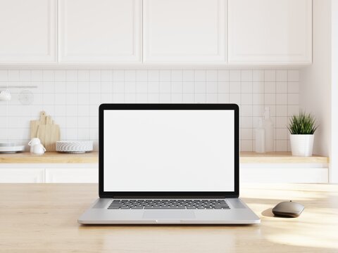 Open laptop with white screen for adding your content. Wooden desk in kitchen with counter in background.. 3D illustration.