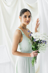 cheerful woman in dress holding bouquet of flowers on white