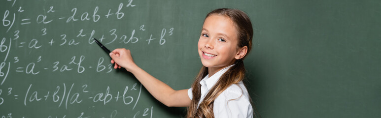 schoolgirl smiling at camera while pointing at equations on chalkboard, banner