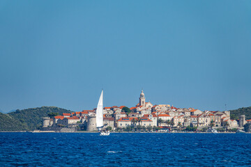 Fototapeta na wymiar AERIAL: Sailboat sails towards the distant ancient town of Korcula, Croatia.