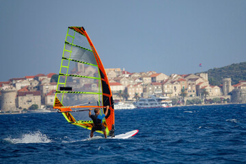 Unrecognizable man windsurfs past the ancient old town of Korcula, Croatia.