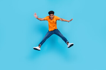 Full body photo of cool brunet young guy jump wear orange t-shirt jeans isolated on blue color background