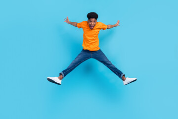 Fototapeta na wymiar Full size photo of hooray brunet young guy jump yell wear orange t-shirt jeans isolated on blue color background