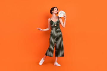 Full body photo of young girl happy positive smile hold money cash dollars rich isolated over orange color background