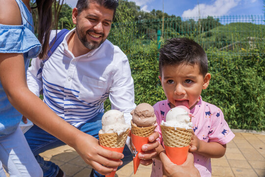 Young Cheerful Hispanic Family Eating Ice Cream In A Park On A Sunny DayCheerful Hispanic Woman Holding A Phone Up In The Air And Running In A Field On A Sunny Day