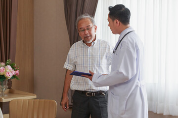 Young Asian doctor standing talking to senior Asian man indoor at the hospital