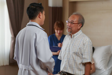 Fototapeta premium Young Asian doctor standing talking to senior Asian man indoor at the hospital.