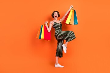 Full body profile side photo of young girl happy positive smile rejoice hold shopping bags isolated over orange color background