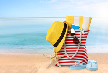 Stylish bag with different accessories on sandy beach, space for text