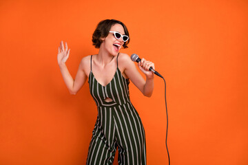 Photo of young attractive girl happy positive smile sing microphone karaoke isolated over orange...