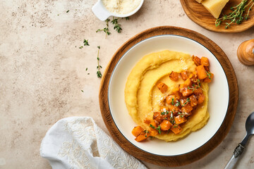 Polenta with butter, pumpkin, garlic, savory and parmesan cheese in white bowl on light concrete background. Traditional Basic Italian food, vegan food. Top view. Copy space.