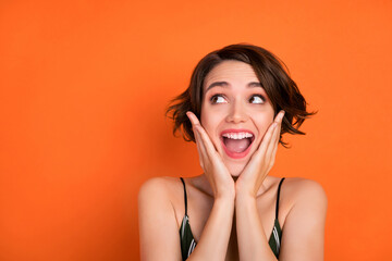 Photo of young girl amazed shocked surprised omg wow happy positive smile look empty space isolated over orange color background
