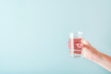 Glass of clean water is held by female hand on a blue background. Selective focus. Mock up. Copy...