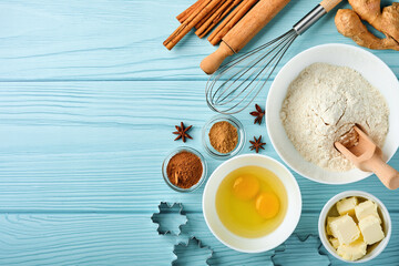 Baking background with ingredients for making gingerbread flour, eggs, kitchen tools, utensils and cookie molds on blue wooden table. Top view. Flat lay style. Mock up. Christmas baking.