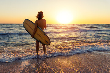 Back view young adult slim sporty female surfer girl with surfboard silhouette stand at ocean coast...