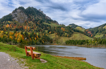 Autumn, bench on the shore Schwarzsee lakes in the eastern foothills of the Alps (Foralpen) - the dark waters of the Schwarzsee lake and the alpine Brekka Abis valley, formed by glaciers. © iravi