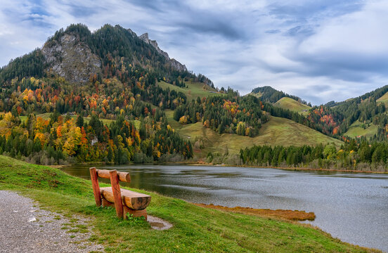 Autumn, bench on the shore Schwarzsee lakes in the eastern foothills of the Alps (Foralpen) - the dark waters of the Schwarzsee lake and the alpine Brekka Abis valley, formed by glaciers.