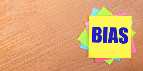 On a wooden table, multi-colored stickers with the text BIAS. Copy space