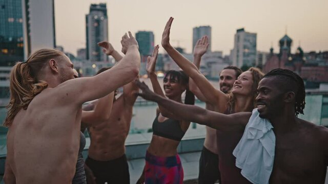 Multiracial group of athletes, men and women in sports uniforms doing a high five after completing a morning workout together. Doing sport on the sttreet. Group high five