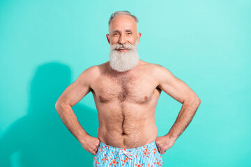 Portrait of attractive cheerful grey-haired bearded man swimmer hands on hips isolated over bright teal turquoise color background
