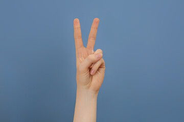 Woman showing two fingers on pale blue background, closeup