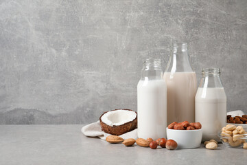 Different nut milks on light grey table. Space for text