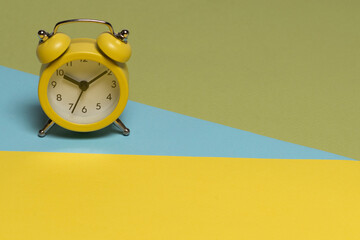 Yellow alarm clock on a yellow, blue and green background. Time concept.