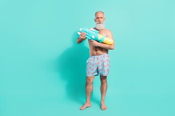 Full length body size view of attractive funky bearded man holding water toy isolated over bright teal turquoise color background