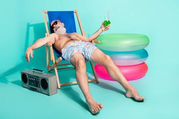 Photo of drunk funny pensioner shirtless lying beach chair drinking alcohol listening boom box...