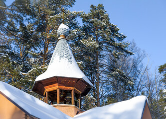 Wooden Christian bell tower with a dome and a cross covered with snow on the background of the forest