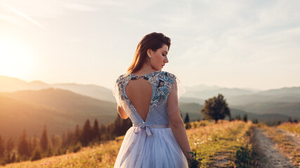 Beautiful bride in blue wedding dress with embroidery and bare back walking in mountains at sunset.