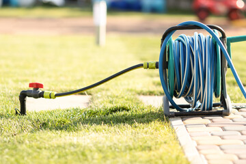A hose rolled onto a reel for watering lawns against a background of clipped green grass on a...