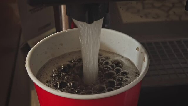 Pouring soft drink soda cola into the paper cup using machine