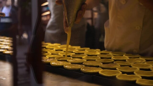 pastry chef behind the counter makes and fills traditional Portuguese pastel de nata pastries with custard