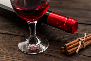 Bottle of red wine with a glass of red wine and  cinnamon sticks tied with jute rope on an old wooden table. Close up view, focus on the glass of red wine
