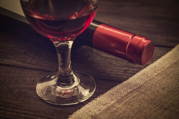 Bottle of red wine with a glass of red wine and piece of canvas on an old wooden table. Close up view, focus on the glass of red wine