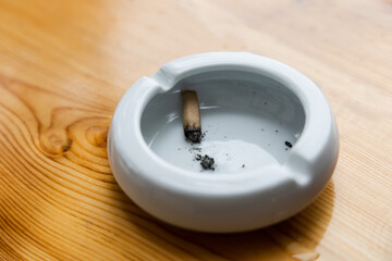 Cigarette stubs and ash in a glass ashtray on wooden table