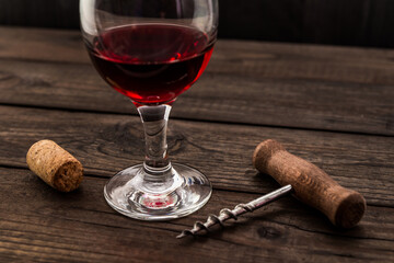 Glass of red wine and corkscrew with cork on an old wooden table. Angle view
