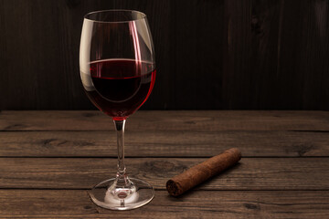 Glass of red wine and cuban cigar on an old wooden table. Focus on the cuban cigar