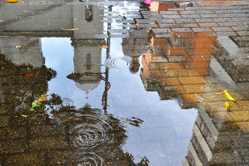 Water reflection after rain in the city where unrecognizable passers-by and a church are seen