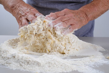 Female hands of an elderly woman knead the dough on a gray table.  Senior woman in a gray apron preparation of dough for a pizza, bread, pasta, festive cake. 